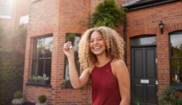 Portrait Of Excited Young Woman Standing Outside New Home Holding Keys
