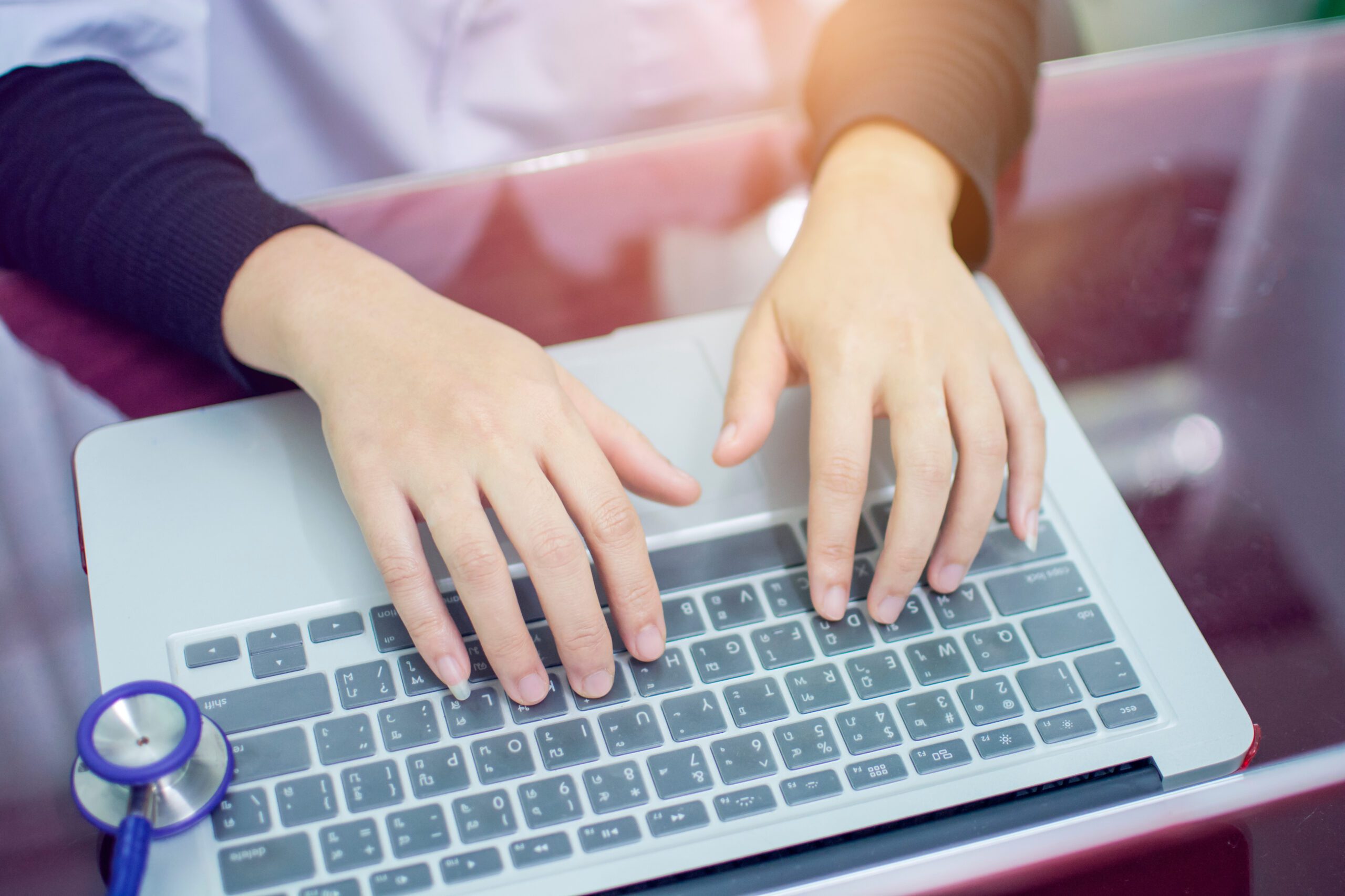 Doctor woman hand typing the Thai keyboard of notebook at the desk for working with blurred of. stethoscope at the hospital office, medical technology concept