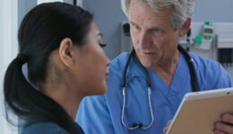 Doctor showing tablet computer with results to patient in hospital exam room