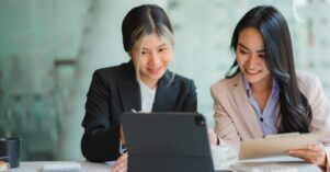 Two Asian business women working together using digital tablets discussing new startup project ideas. Analyze the planning and statistics of the financial and investment markets at the office. Two Asian business women working together using digital tablets discussing new startup project ideas. Analyze the planning and statistics of the financial and investment markets at the office.