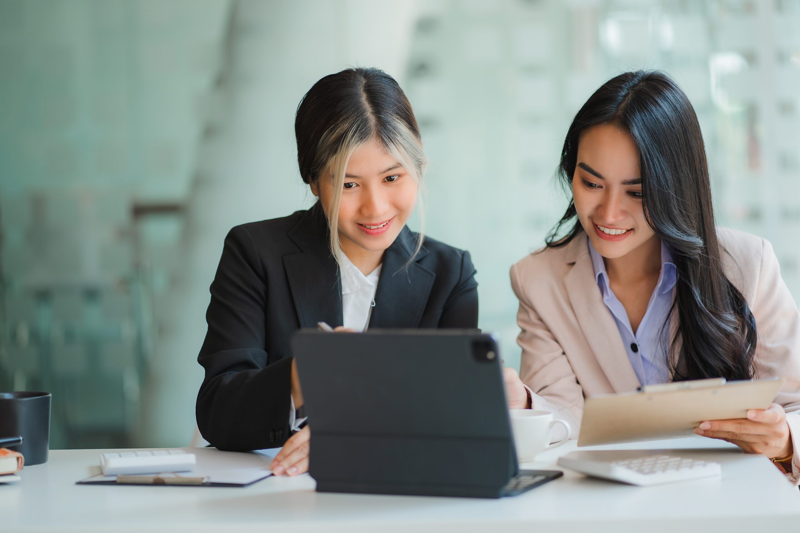 Two Asian business women working together using digital tablets discussing new startup project ideas. Analyze the planning and statistics of the financial and investment markets at the office.