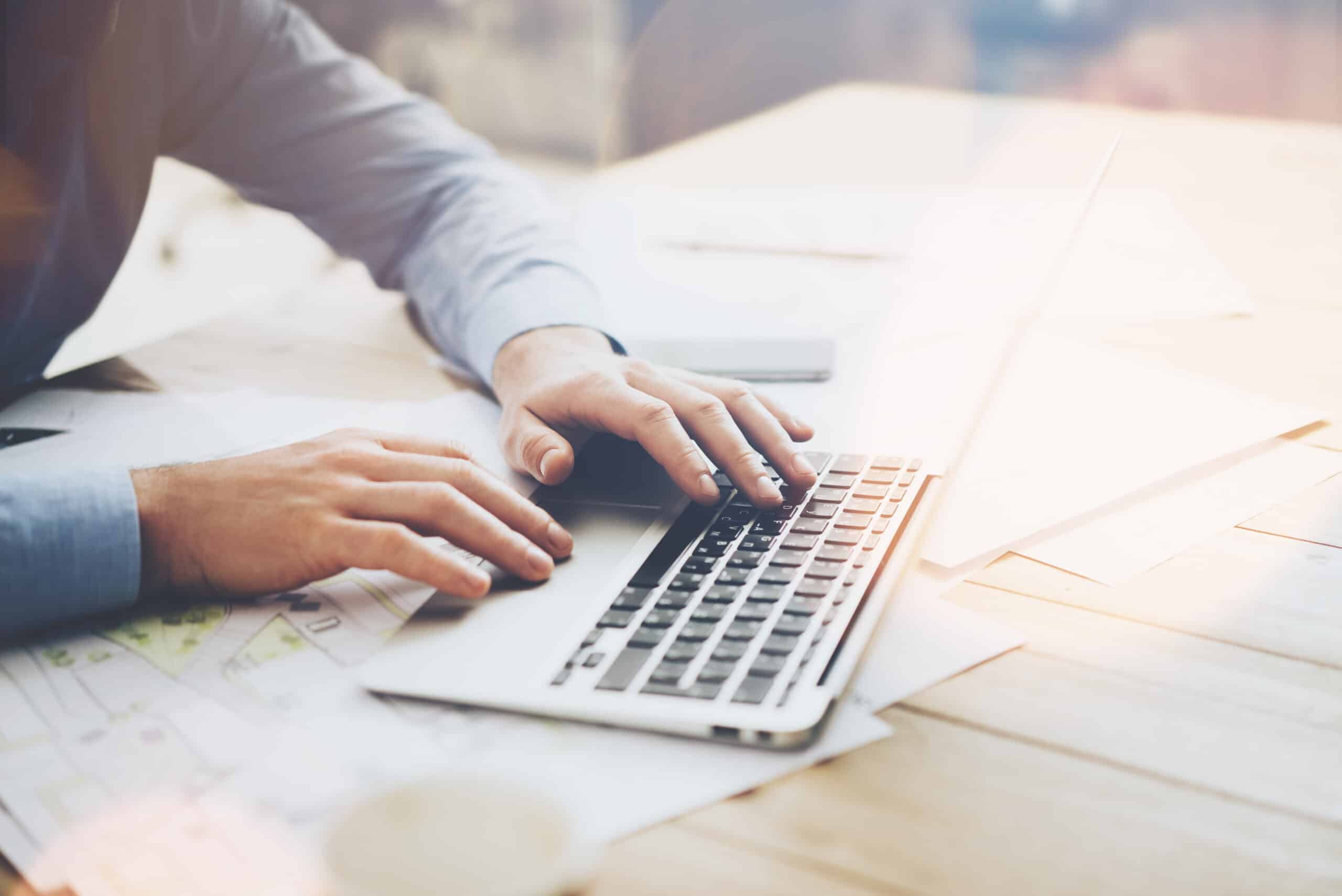 Photo businessman working on modern loft office. Man sitting wood table and using contemporary notebook, texting message keyboard. Horizontal, film effect Boosting enterprise efficiency through Managed IT services and proactive IT monitoring
